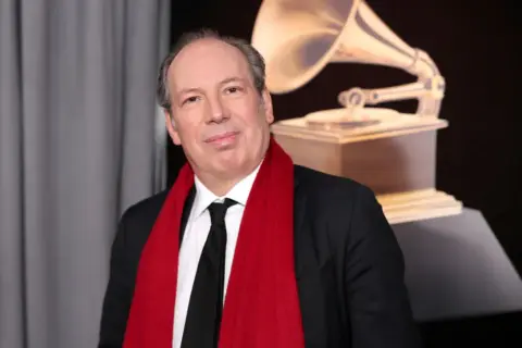 Hans Zimmer, który napisał muzykę do filmu Gladiator, pozuje z czerwoną szarfą i statuetką Grammy.