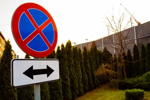 Znak zakazu zatrzymywania się i postoju, z tabliczką wskazującą kierunki. Uważaj, bo grozi za to mandat.