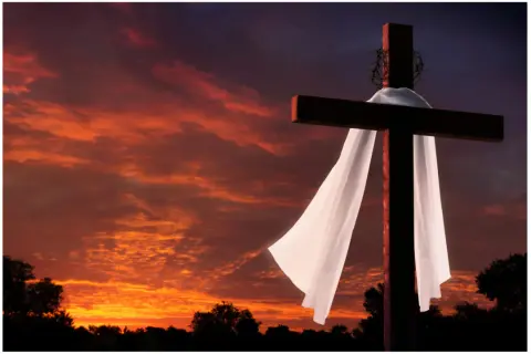 Kreuz mit Dornenkrone und Leichentuch vor dramatischem Sonnenuntergang. Ein Symbol für Karfreitag, den Feiertag der Besinnung.