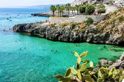 Scogliera con mare cristallino e gente che nuota, tipica dei paesi sul mare in Puglia.