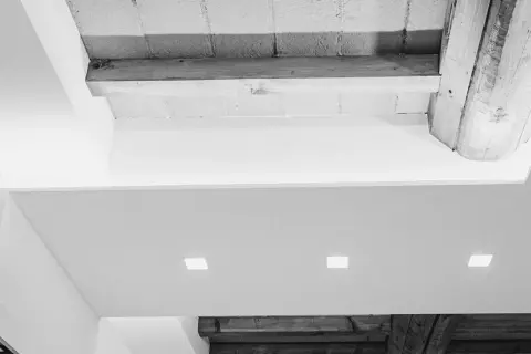 Soffitto con faretti incassati e travi a vista. Una moderna colonna cartongesso con nicchie illumina l'ambiente.