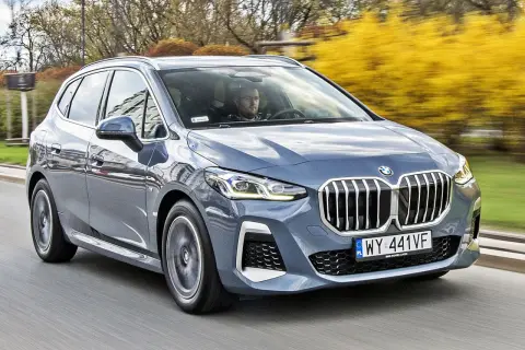 Szary BMW 2 Active Tourer jedzie po drodze, za nim widać żółte krzewy.