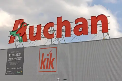 Duże czerwone logo Auchan z ptaszkiem, poniżej banery sklepów Floraria Rhapsody i Kik. Aplikacja Auchan ułatwia zakupy.