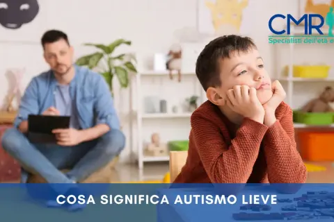 Bambino pensieroso in terapia, con un uomo sullo sfondo. Si parla di autismo lieve e della sua percentuale di invalidità.