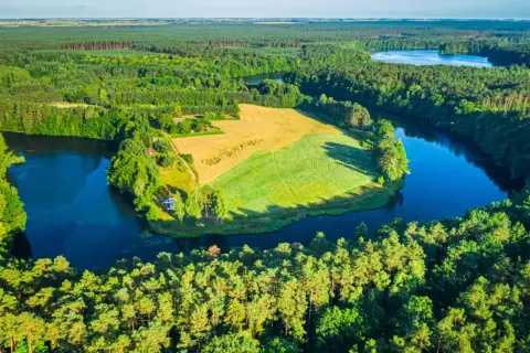 Malownicze Bory Tucholskie z lotu ptaka: ciemne jezioro otoczone gęstym lasem, pole uprawne i niewielka osada.