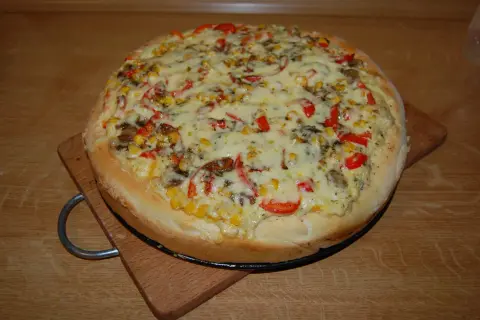 Pizza z kukurydzą, papryką i grzybami, polana obficie białym sosem do pizzy, na drewnianym blacie.