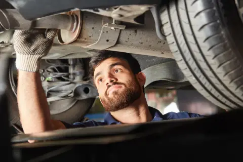 Mechanik w rękawiczce sprawdza podwozie samochodu, wykonując naprawę układu wydechowego.