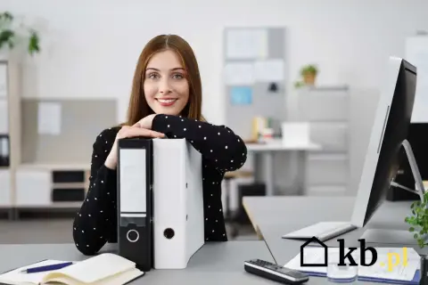 Uśmiechnięta kobieta w biurze opiera się o segregator.
