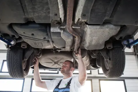 Mechanik sprawdza podwozie sedana na podnośniku, badając układ wydechowy i zawieszenie.