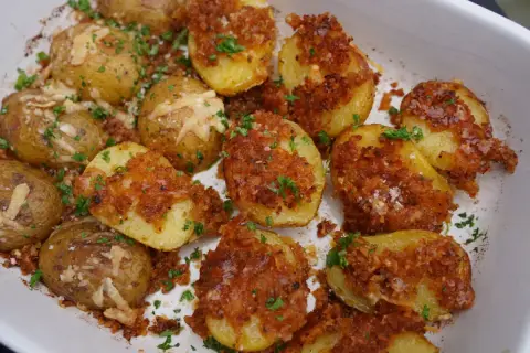 Knusprige parmesan kartoffeln mit Petersilie und grobem Salz bestreut, bereit zum Genießen.