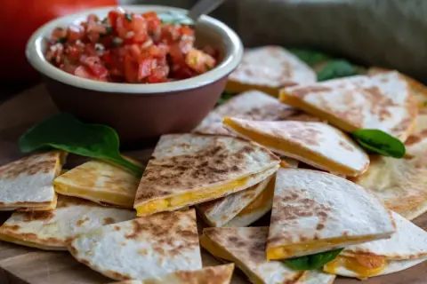 En hög med gyllene, ostiga quesadillas, perfekta för ett snabbt quesadillas recept. Serveras med en skål färsk pico de gallo.