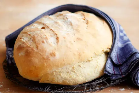 Frisch gebackenes Brot, das nach dem **Brot selber backen** auf einem Gitter abkühlt. Ein blau-weißes Tuch umhüllt es.