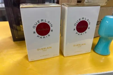 Dwie białe perfumy Samsara Guerlain 75 ml, każda w złotym opakowaniu, stoją na żółtej powierzchni.