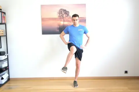 Homme effectuant un exercice de rotation interne hanche, jambe levée, mains sur les hanches.