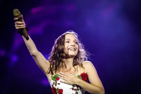 Sanah śpiewa "Bujda" na koncercie, trzymając złoty mikrofon i dotykając serca.