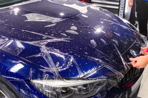 Niebieski **car color** z folią ochronną na masce. Widać krople wody i pęcherzyki powietrza pod folią.