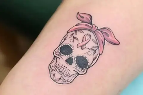 Calavera adornada con lazo rosa y cinta de concienciación, símbolo de tatuajes de superación cáncer.