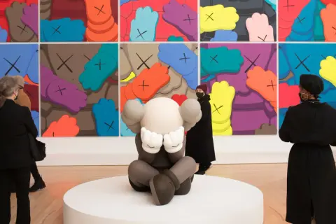 A KAWS sculpture sits before a vibrant mural, inspiring KAWS painting ideas. Visitors admire the art.