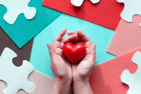 Mani che stringono un cuore rosso, circondate da pezzi di puzzle bianchi e sfondi colorati. Un gesto d'amore, perché si può fare una donazione tra fratelli.