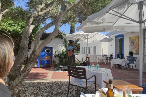 Un músico toca la guitarra en el patio de el pozo de los frailes restaurantes. Mesas puestas bajo sombrillas blancas invitan a disfrutar.