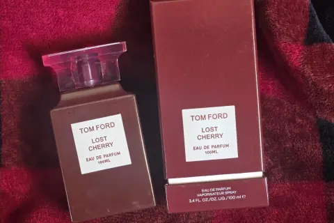 Elegancki flakon i pudełko perfum Tom Ford Lost Cherry 100 ml na tle czerwonego, miękkiego materiału.