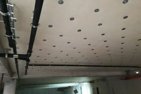 Sufit w garażu z widocznymi rurami kanalizacyjnymi i licznymi okrągłymi elementami mocującymi.