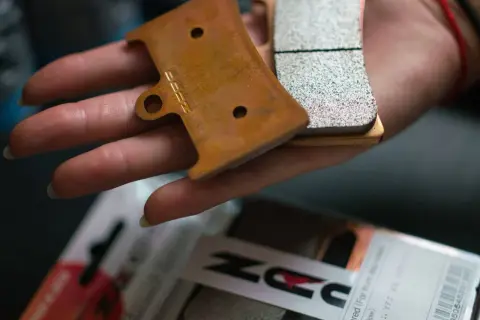 Main d'une personne tenant des plaquettes de frein neuves, prêtes pour le rodage. Le logo "DZ" est visible sur l'une d'elles.