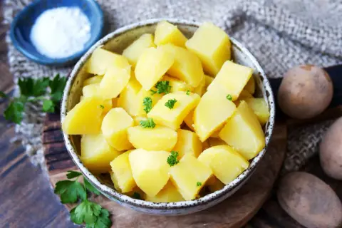 Schüssel mit dampfenden Salzkartoffeln, garniert mit Petersilie. Daneben eine kleine Schale Salz und rohe Kartoffeln.