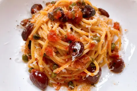 Ein Teller Spaghetti Puttanesca, garniert mit Oliven, Kapern und geriebenem Parmesan.