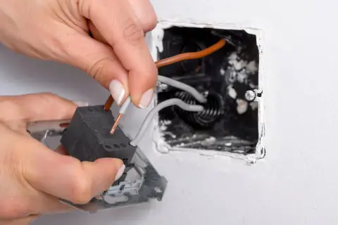 Manos conectando cables a un interruptor conmutador dentro de una caja empotrada en la pared.