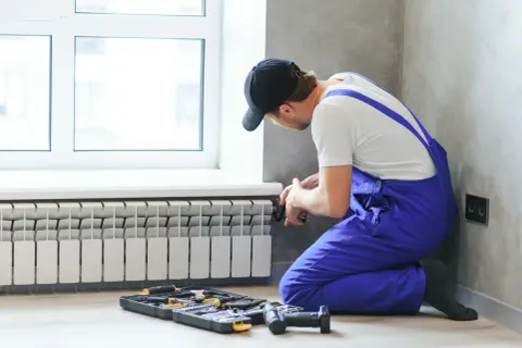 Instalator wykonuje podłączenie grzejnika od dołu. Obok leżą narzędzia.