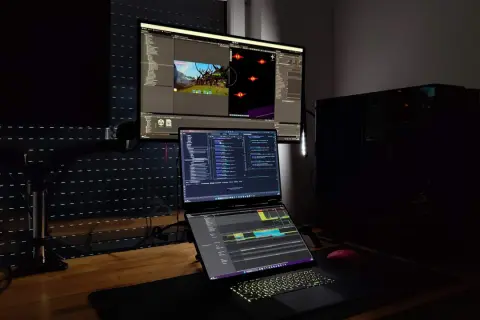 Stanowisko programisty z trzema monitorami, na których widać edytor kodu i scenę gry. Czy c.