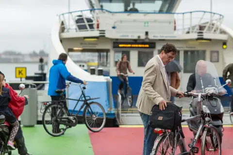 Man met fiets op veerboot, een ongeluk fietser in de verte.