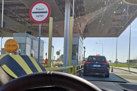 Kolejka samochodów na autostradzie A4 przed punktem poboru opłat. Widać bramki, znaki drogowe i samochody czekające na przejazd.