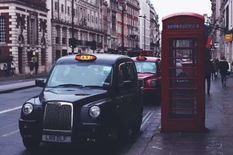 Czarne taksówki i czerwona budka telefoniczna na ulicy w Londynie.