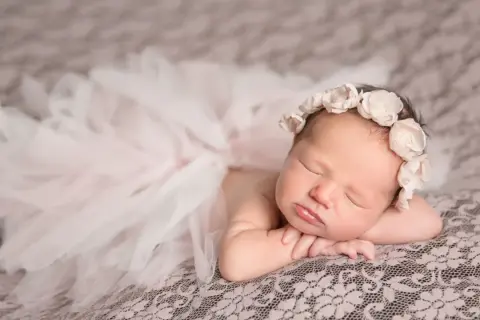Un bébé endormi, paré d'une couronne de fleurs et d'une jupe en tulle, évoque la douceur et la pureté. Sa pose paisible invite à réfléchir à la signification prénom.