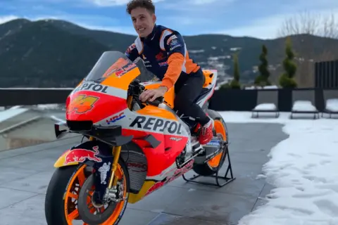 Piloto de Honda MotoGP con su moto Repsol, listo para la temporada, con montañas nevadas de fondo.
