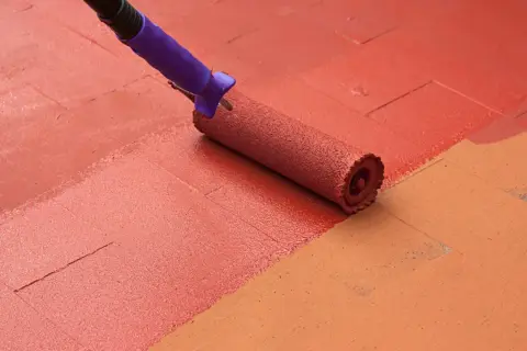 Rodillo aplicando pintura para suelos de exterior de color rojo sobre baldosas.