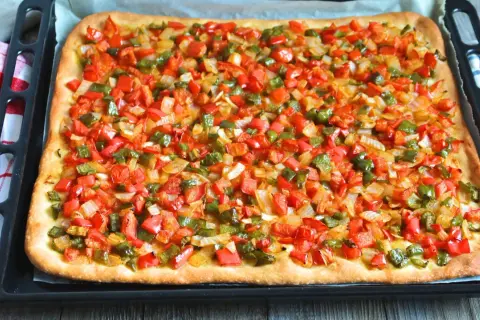 Coca mallorquina recién horneada, cubierta con pimientos rojos y verdes picados y cebolla.