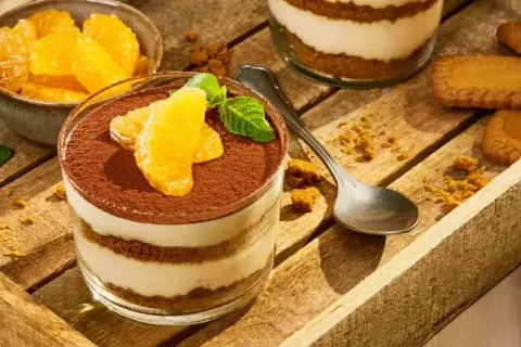 Délicieux tiramisu aux fruits d'orange, garni de cacao et de menthe fraîche, servi dans un verre sur un plateau en bois avec des biscuits.