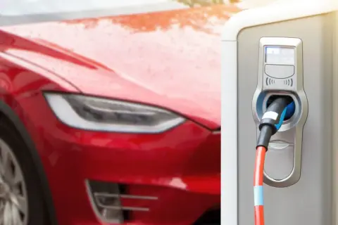 Czerwona Tesla podłączona do ładowarki. Zastanawiasz się, jak długo ładuje się Tesla? Czas zależy od modelu i ładowarki.