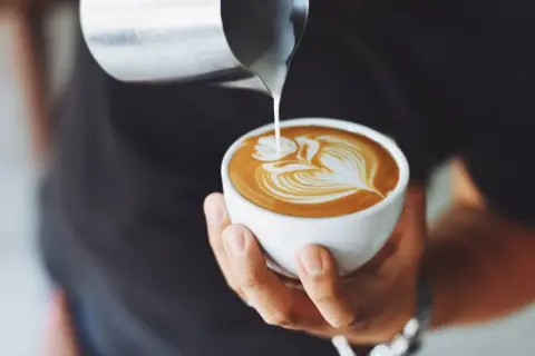 Barista versa latte art su un cappuccino, mostrando come si fa il cappuccino con maestria.