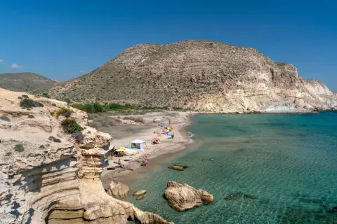 La cala del Peñón Blanco, con su arena dorada y aguas cristalinas, invita a disfrutar del sol bajo un cielo azul.