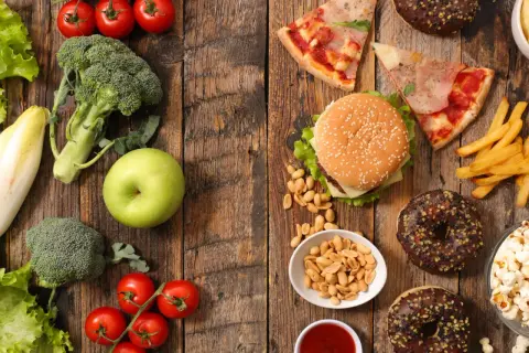 Gesunde Lebensmittel wie Brokkoli, Tomaten und ein Apfel stehen im Kontrast zu Junkfood wie Pizza, Burger, Pommes und Donuts.