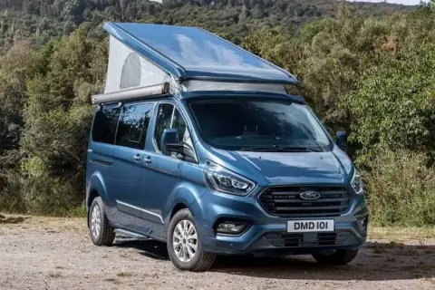 Furgoneta camper azul Westfalia Nugget con techo elevable, lista para una aventura en la naturaleza.