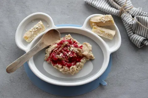 Leckerer Morgenbrei für Babys mit Beeren und Bananenstückchen auf einem Teller in Bärenform.