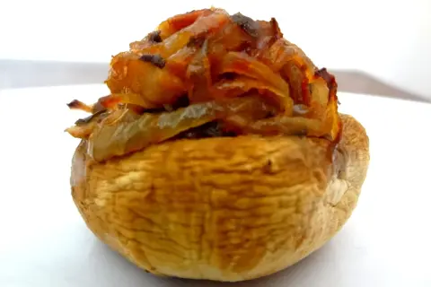 Gros plan sur un champignon farci, garni d'oignons caramélisés et d'herbes. Un délice à savourer !