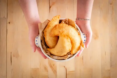Mani che offrono un cestino di frittelle dorate, un sapore autentico di street food pugliese.