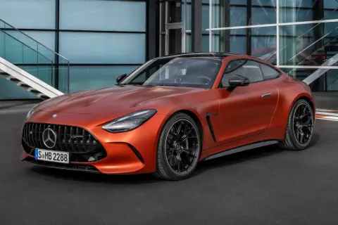 Pomarańczowy Mercedes-AMG GT 63 z czarnymi felgami stoi przed nowoczesnym budynkiem z przeszkloną fasadą i schodami.