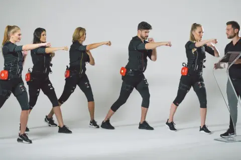 Grupa osób w strojach EMS ćwiczy pod okiem trenera. Dowiedz się, ile kosztuje trening EMS i zacznij swoją metamorfozę!